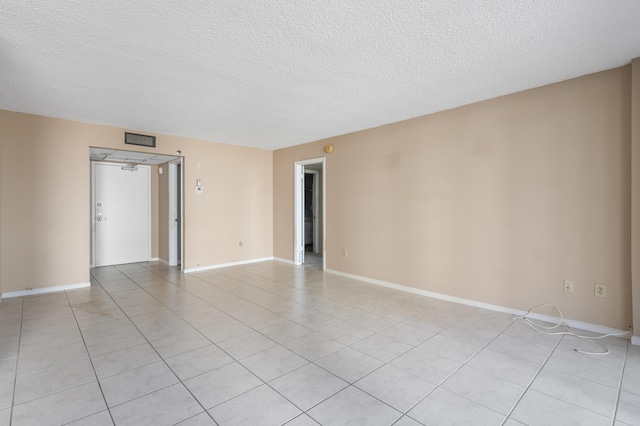 empty room with a textured ceiling, light tile patterned floors, and baseboards