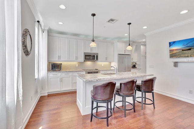 kitchen featuring stainless steel appliances, white cabinetry, hanging light fixtures, and a center island with sink