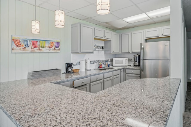 kitchen featuring hanging light fixtures, kitchen peninsula, a paneled ceiling, and stainless steel refrigerator