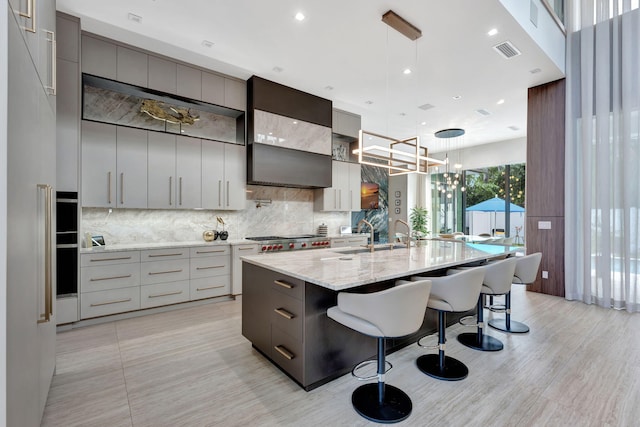 kitchen featuring a large island with sink, a kitchen breakfast bar, gray cabinetry, backsplash, and pendant lighting