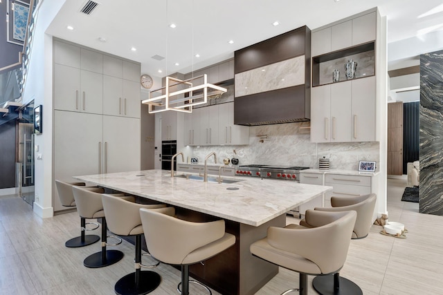 kitchen featuring pendant lighting, gray cabinetry, custom exhaust hood, and an island with sink