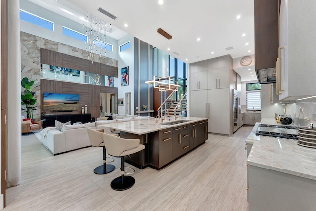 kitchen with a towering ceiling, sink, hanging light fixtures, a breakfast bar area, and a center island with sink