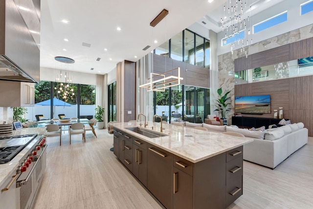 kitchen featuring a spacious island, a high ceiling, wall chimney exhaust hood, hanging light fixtures, and sink