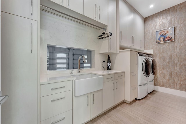 laundry area with sink, independent washer and dryer, light wood-type flooring, and cabinets