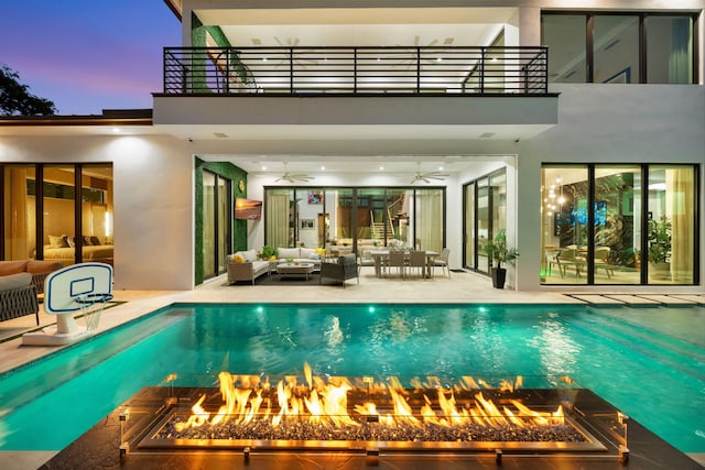 pool at dusk featuring a patio, an outdoor living space with a fire pit, and ceiling fan