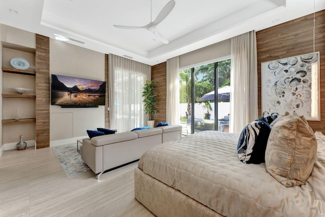 bedroom with wood walls, ceiling fan, access to exterior, and a raised ceiling