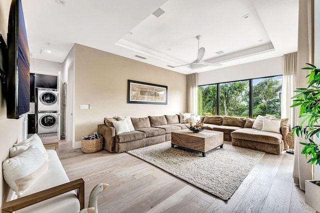 living room with light hardwood / wood-style flooring, ceiling fan, stacked washer and clothes dryer, and a raised ceiling