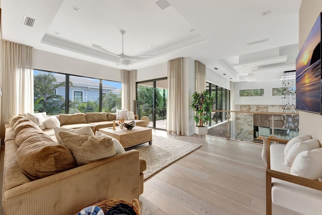 living room featuring a fireplace, a tray ceiling, light wood-type flooring, and ceiling fan