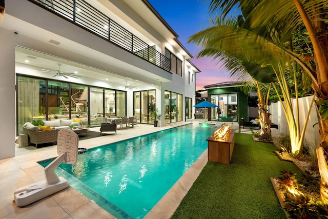 pool at dusk with a patio area, outdoor lounge area, and ceiling fan