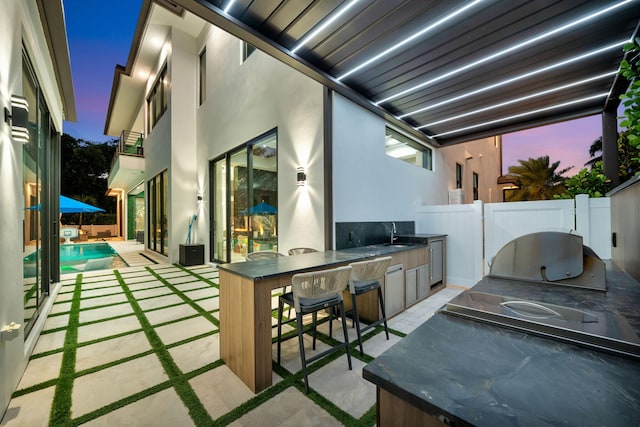 patio terrace at dusk with a fenced in pool, exterior kitchen, sink, and a balcony