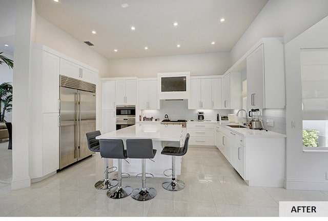 kitchen featuring light stone countertops, sink, light brown cabinets, built in appliances, and a kitchen island