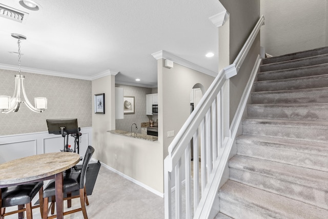 stairs with a textured ceiling, sink, crown molding, and a notable chandelier