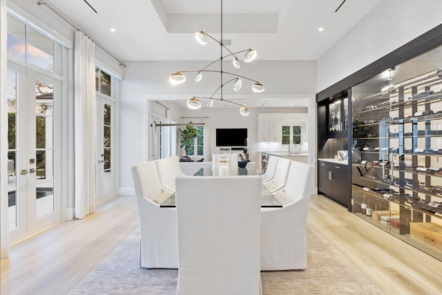 dining room with a chandelier, light hardwood / wood-style flooring, french doors, and a raised ceiling