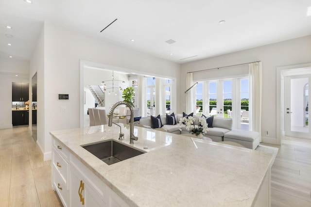 kitchen with white cabinetry, an island with sink, sink, light stone countertops, and french doors