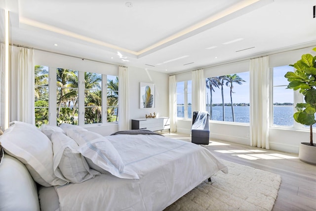 bedroom with a tray ceiling, light hardwood / wood-style floors, and a water view