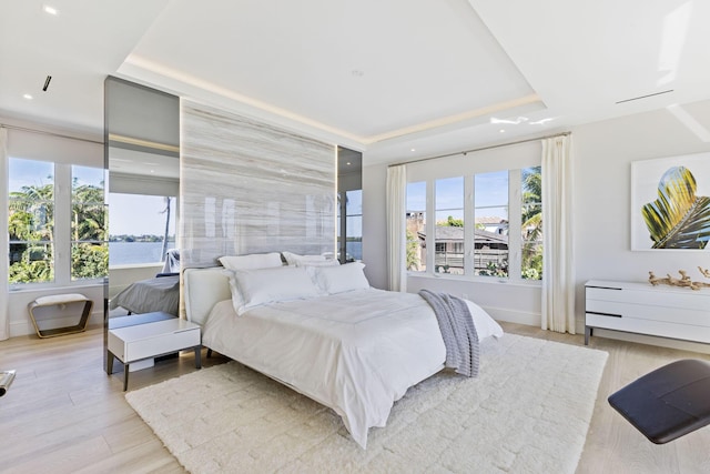 bedroom featuring a raised ceiling, baseboards, and light wood finished floors