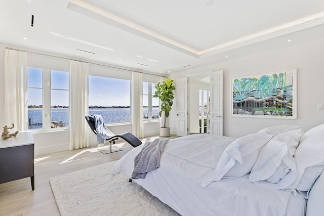 bedroom featuring recessed lighting, a raised ceiling, a water view, and light wood finished floors