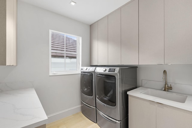 clothes washing area featuring washer and clothes dryer, light wood finished floors, cabinet space, a sink, and baseboards