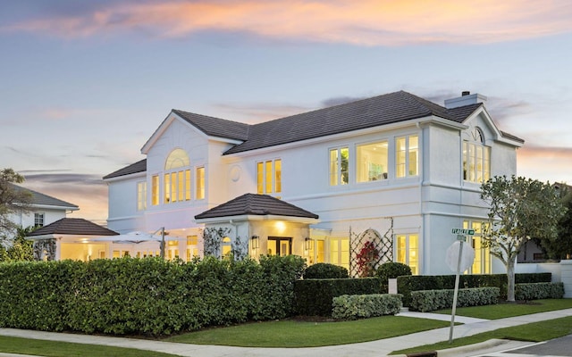 view of front of house featuring a tiled roof, a yard, a chimney, and stucco siding