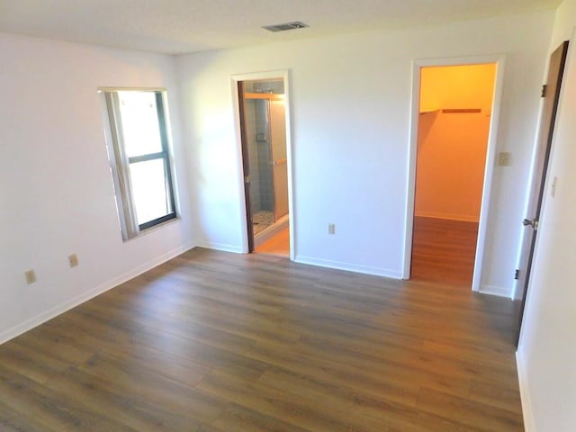 unfurnished bedroom featuring ensuite bath, a spacious closet, and dark wood-type flooring