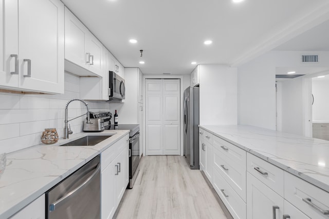 kitchen with sink, light hardwood / wood-style floors, stainless steel appliances, white cabinets, and light stone counters