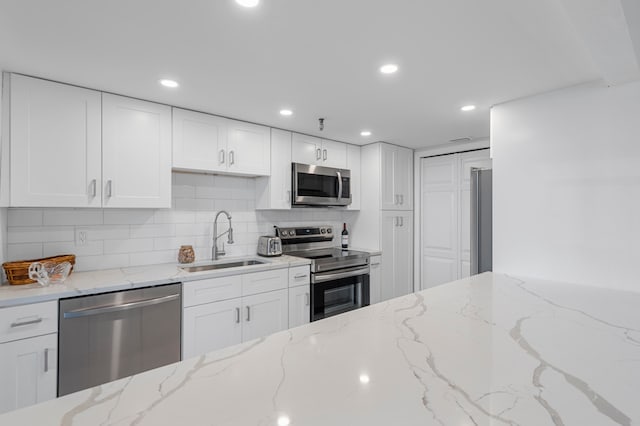 kitchen featuring white cabinets, light stone counters, backsplash, sink, and stainless steel appliances