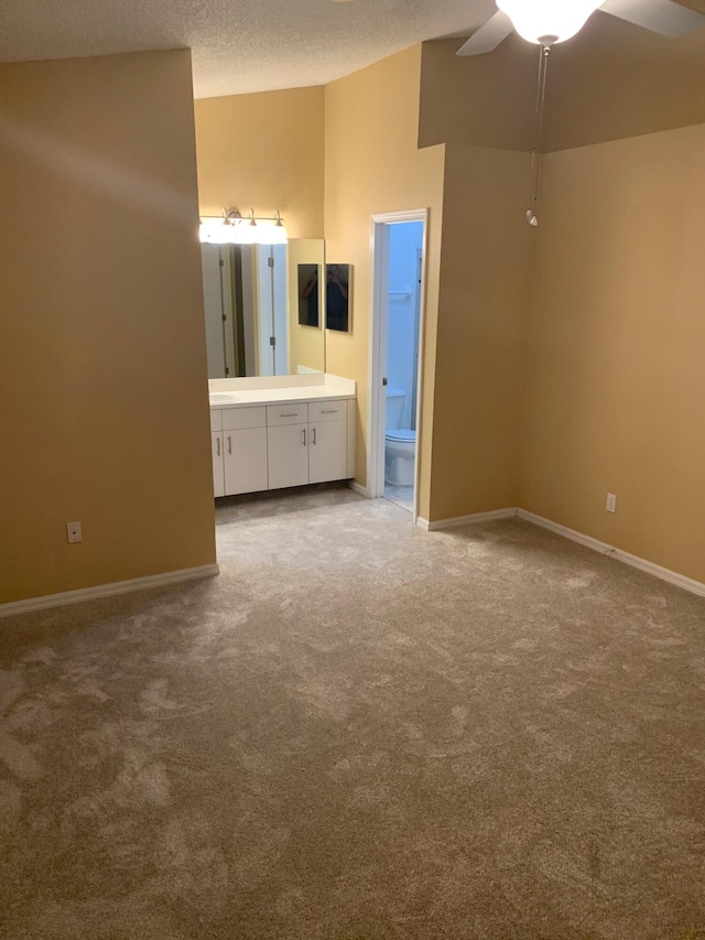 unfurnished bedroom with ceiling fan, a textured ceiling, carpet floors, and ensuite bath