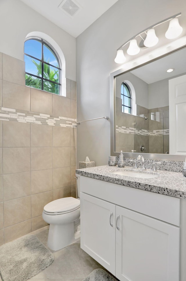 bathroom with tile patterned flooring, vanity, toilet, and tile walls