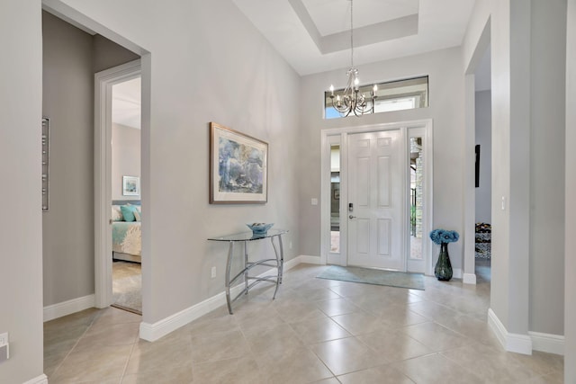 foyer entrance featuring light tile patterned flooring, a high ceiling, a tray ceiling, and an inviting chandelier