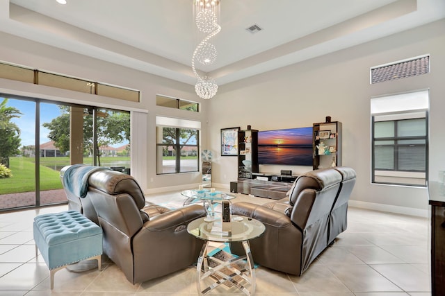 tiled living room featuring a tray ceiling, a high ceiling, and a notable chandelier