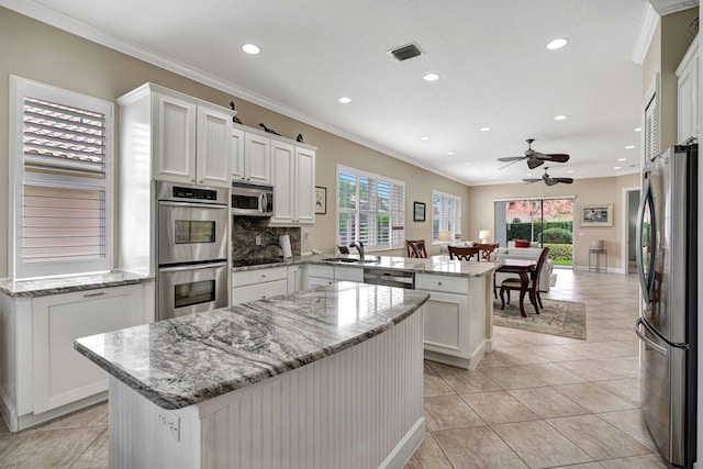 kitchen with white cabinetry, a center island, appliances with stainless steel finishes, kitchen peninsula, and light stone countertops