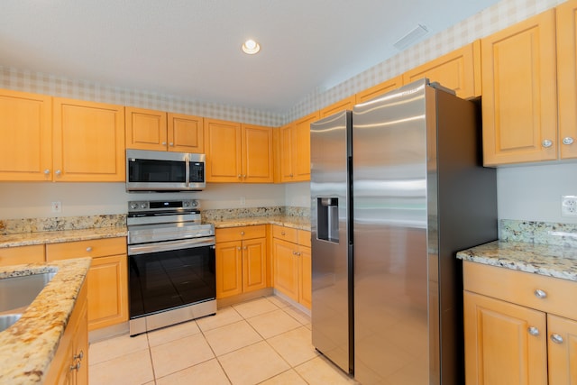 kitchen with light stone counters, stainless steel appliances, light tile patterned floors, and light brown cabinets