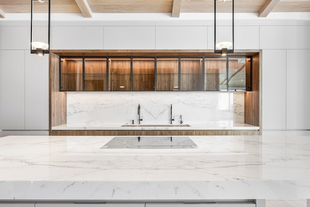 interior space with a sink, modern cabinets, beam ceiling, and light stone counters