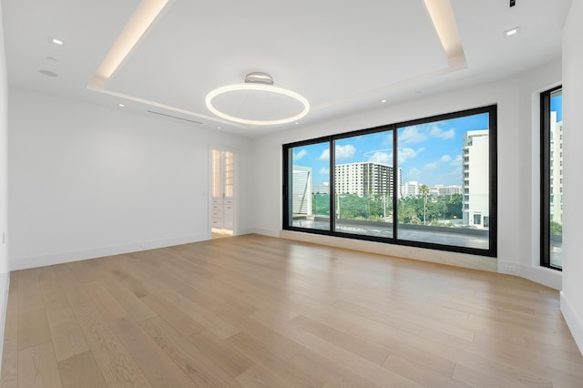 empty room featuring a raised ceiling, baseboards, light wood-style floors, a view of city, and recessed lighting