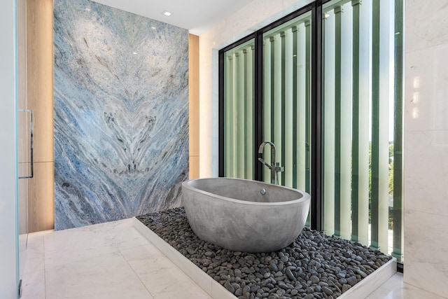 full bath featuring tile walls, marble finish floor, a sink, and a freestanding tub