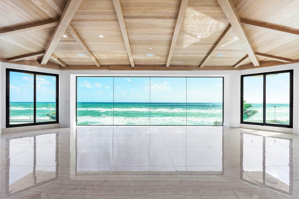 unfurnished room featuring lofted ceiling with beams, a water view, wooden ceiling, and a wealth of natural light