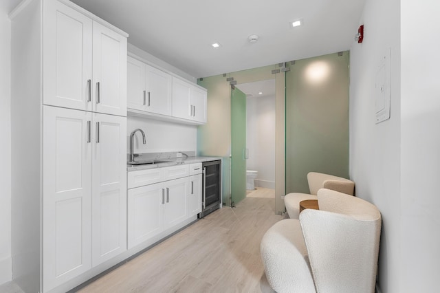 kitchen featuring light stone counters, a sink, white cabinetry, beverage cooler, and light wood-style flooring