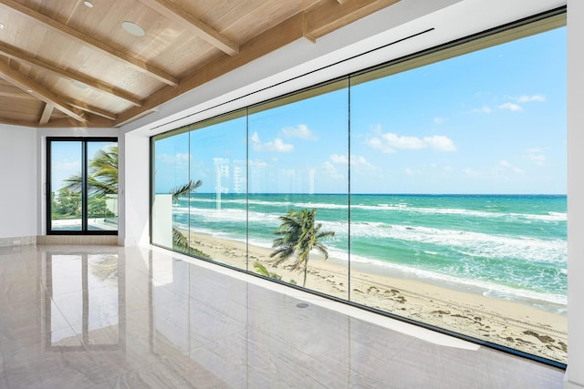 unfurnished sunroom with a view of the beach, beamed ceiling, and a water view