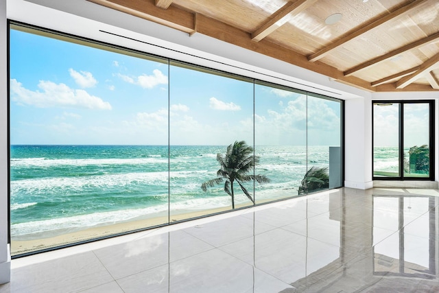 unfurnished sunroom with a water view, a beach view, and beamed ceiling