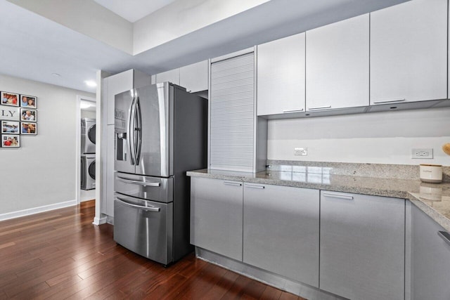 kitchen featuring dark wood-type flooring, light stone counters, white cabinets, stacked washer / dryer, and stainless steel fridge