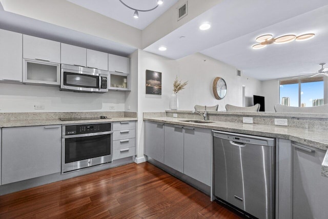 kitchen with stainless steel appliances, dark hardwood / wood-style floors, light stone countertops, sink, and ceiling fan