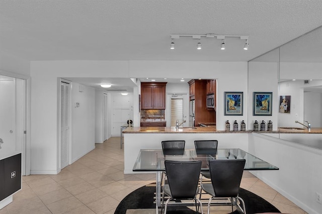 dining area featuring sink, a textured ceiling, rail lighting, and light tile patterned floors