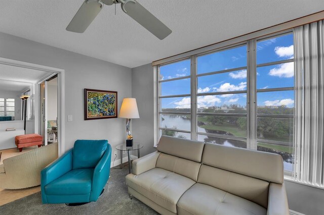 living room with a textured ceiling, carpet flooring, a water view, and ceiling fan