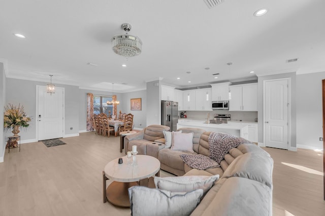 living room with light hardwood / wood-style floors, sink, an inviting chandelier, and ornamental molding