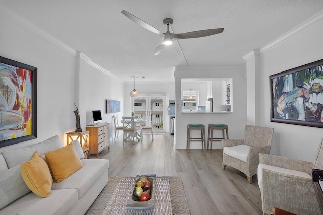 living room with a textured ceiling, ceiling fan, light wood-type flooring, and crown molding