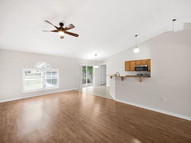 unfurnished living room with vaulted ceiling, ceiling fan, light wood-type flooring, and a wealth of natural light