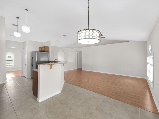 kitchen with kitchen peninsula, a healthy amount of sunlight, light stone counters, and light wood-type flooring