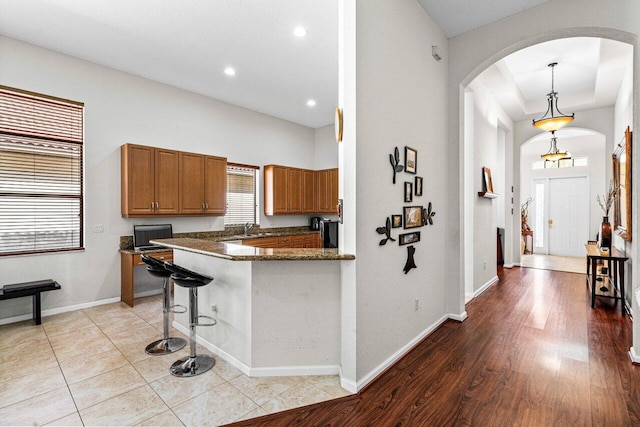 kitchen featuring kitchen peninsula, light wood-type flooring, a breakfast bar, decorative light fixtures, and dark stone countertops