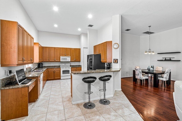 kitchen featuring kitchen peninsula, dark stone counters, white appliances, sink, and light hardwood / wood-style floors