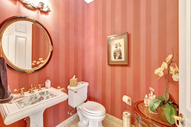 bathroom featuring wallpapered walls, toilet, a sink, tile patterned flooring, and baseboards